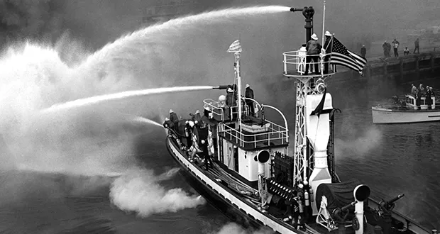 Historic tugboat spraying water in black and white.