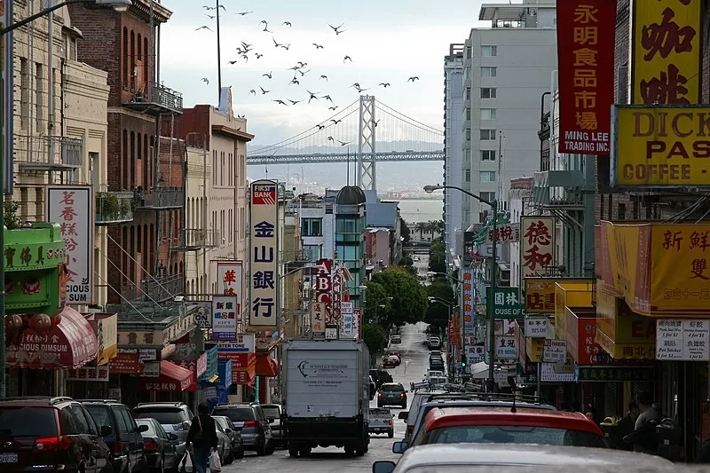 Busy street with Chinese signs and bridge in background.