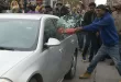 Protestor breaking car window with a bat.