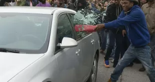 Protestor breaking car window with a bat.