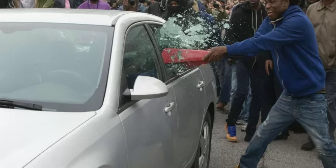 Protestor breaking car window with a bat.