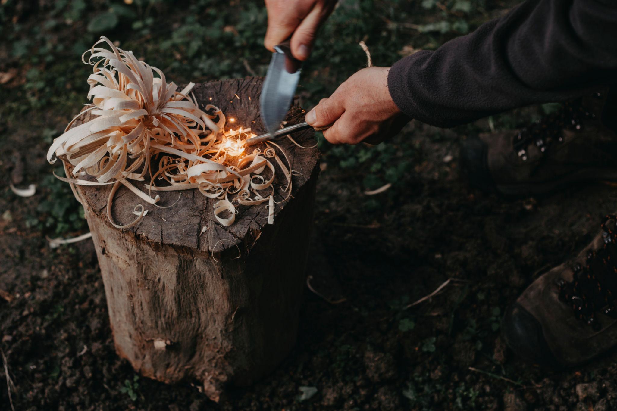 Person creating sparks from wood shavings outdoors.