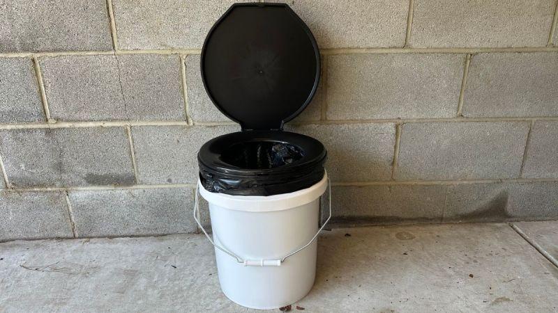 Portable toilet with black lid and white bucket.