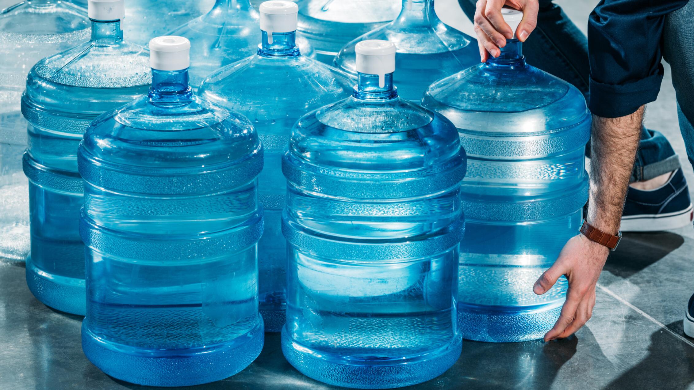 Person handling large blue water jugs.